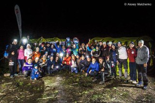 Групповое фото участников и организаторов в темноте у флагов: коллективая фотография после забега с яркими налобными фонарями и палатками на фоне