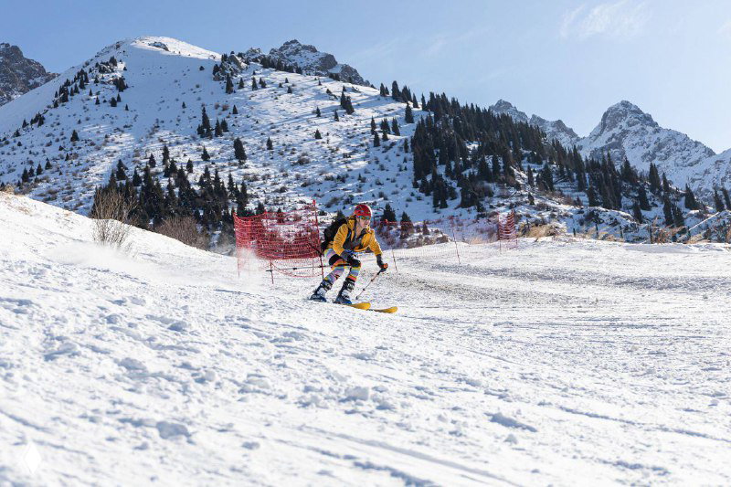 Один из участников на спуске по снежной трассе: спортсмен в экипировке выполняет контролируемый спринт вниз по склону на фоне гор.