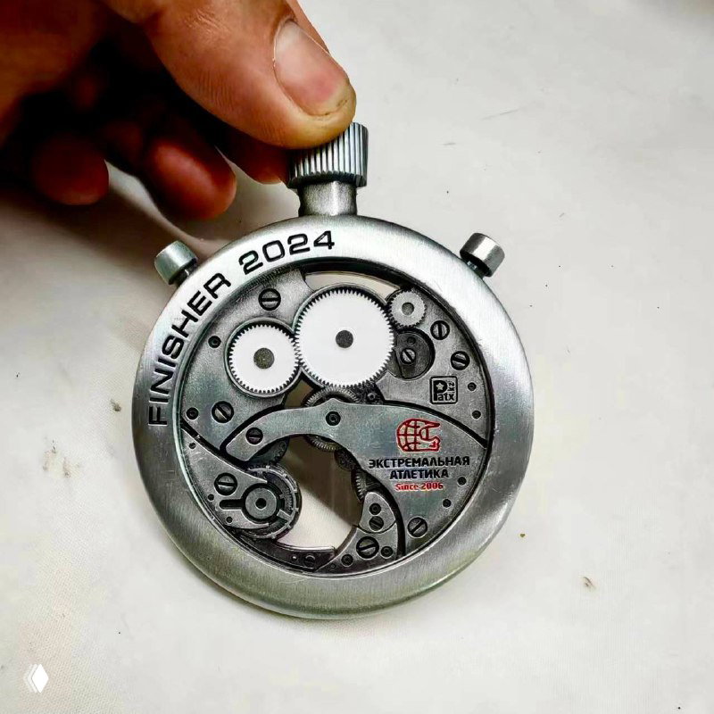 Лицевая сторона медали с гравировкой «FINISHER 2024» и декоративными шестерёнками; крупный план, видны надписи и дизайнерские элементы.