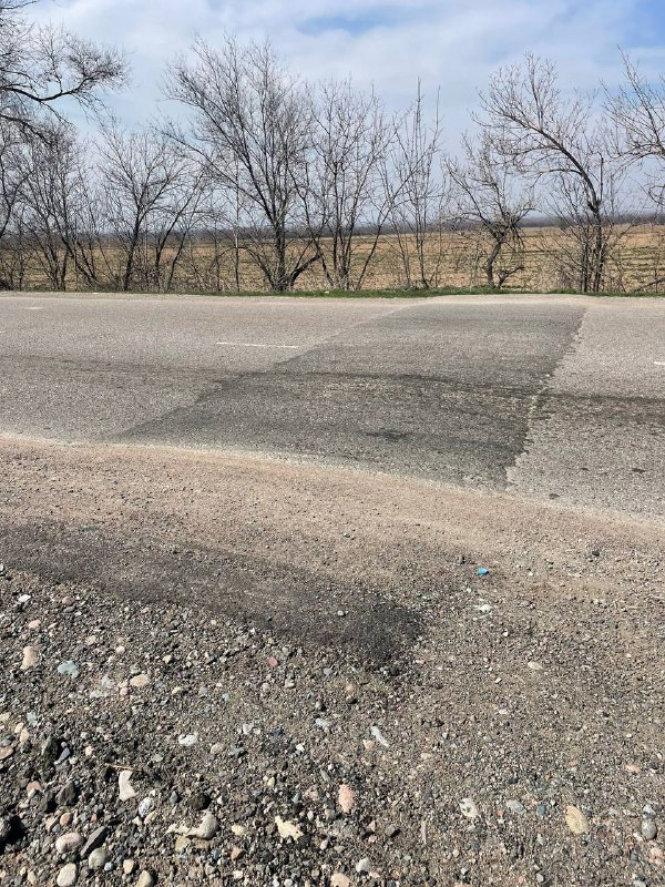 Кадр трассы с заделанными фрагментами асфальта; видно ровные и подлатанные участки, где установлены или будут установлены лежачие полицейские.