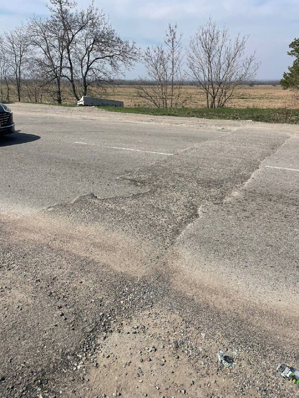 Вид на участок дороги перед разворотом с заплатами на асфальте и автомобилем вдалеке; контекст расположения препятствий на трассе.