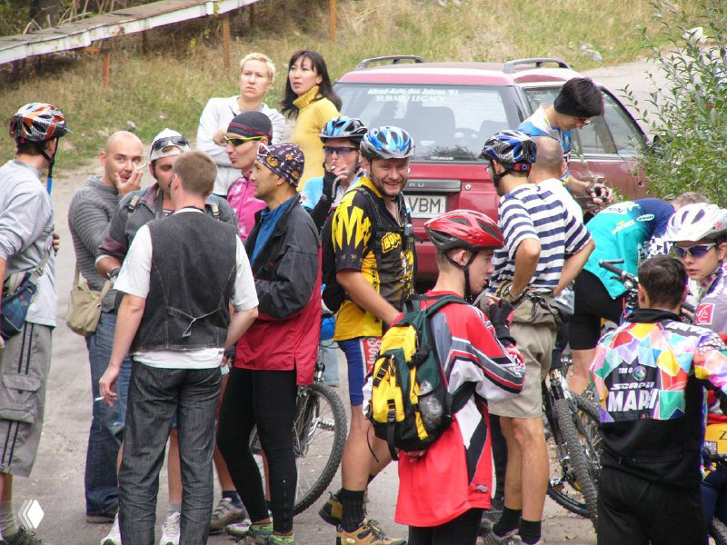 Зрители и участники у зоны регистрации — разноцветные майки, рюкзаки и непринужденная атмосфера перед стартом гонки.