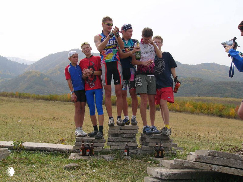 Победители на подиуме — юные участники яблочной гонки позируют с призами на фоне горного пейзажа и полей.