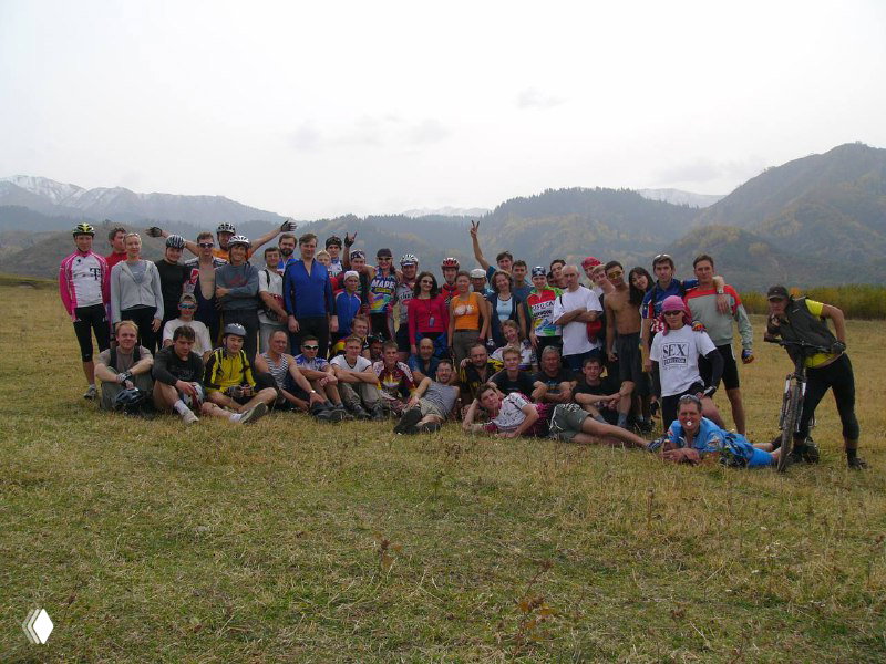 Большая групповая фотография участников Apple Race в поле на фоне холмов и леса — коллективное фото после гонки.