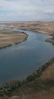 Аэрофотография извилистой реки в Великой степи: широкая водная артерия, холмы и редкие деревья — пейзаж Tengri Ultra.