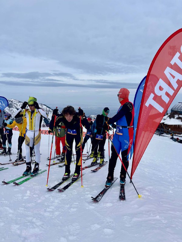 Групповой кадр со стартовавшими спортсменами — мужчины и женщины выстраиваются на трассе перед подъёмом по снежной долине.