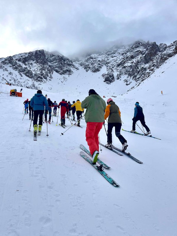Спортсмены поднимаются по снежной тропе в горах Шымбулака во время дисциплины Вертикальный километр; вид на горные вершины и трассу.