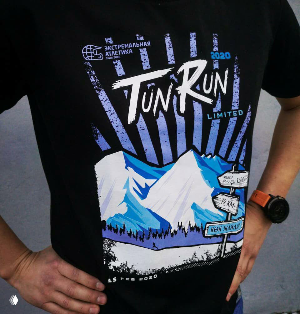Крупный план принта Tun Run на чёрной футболке: изображение гор, указатели маршрута и логотип «Экстремальная Атлетика», видны часы на запястье.