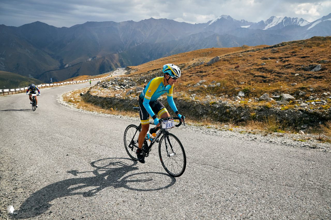 Гонщик на шоссейном велосипеде в яркой форме поднимается по серпантину в горах — типичная сцена велокатегории Kosmos UpHill.