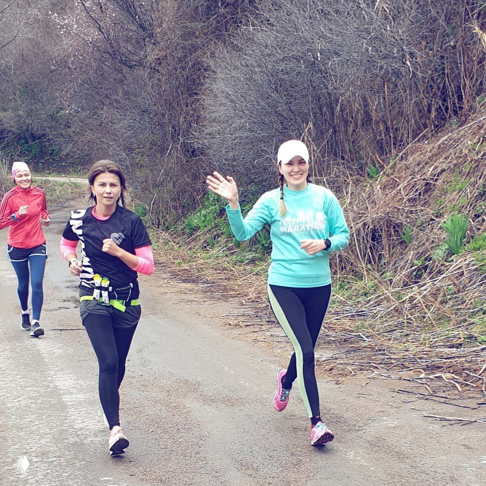 Группа бегуноков по весенней дороге среди кустов и деревьев: улыбающиеся спортсмены в тренировочном забеге перед соревнованиями.