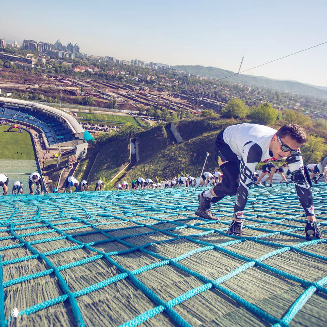 Участники поднимаются по крутой сетке трамплина над стадионом — визуал, хорошо иллюстрирующий сложность трассы Red Bull 400 в Алматы.