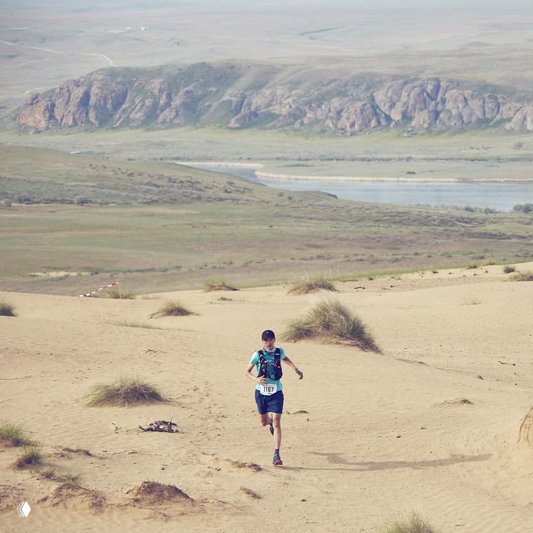 Один бегун преодолевает песчаные барханы и степные участки на берегу реки — типичный кадр с ultramarathon Tengri Ultra в Великой Степи.