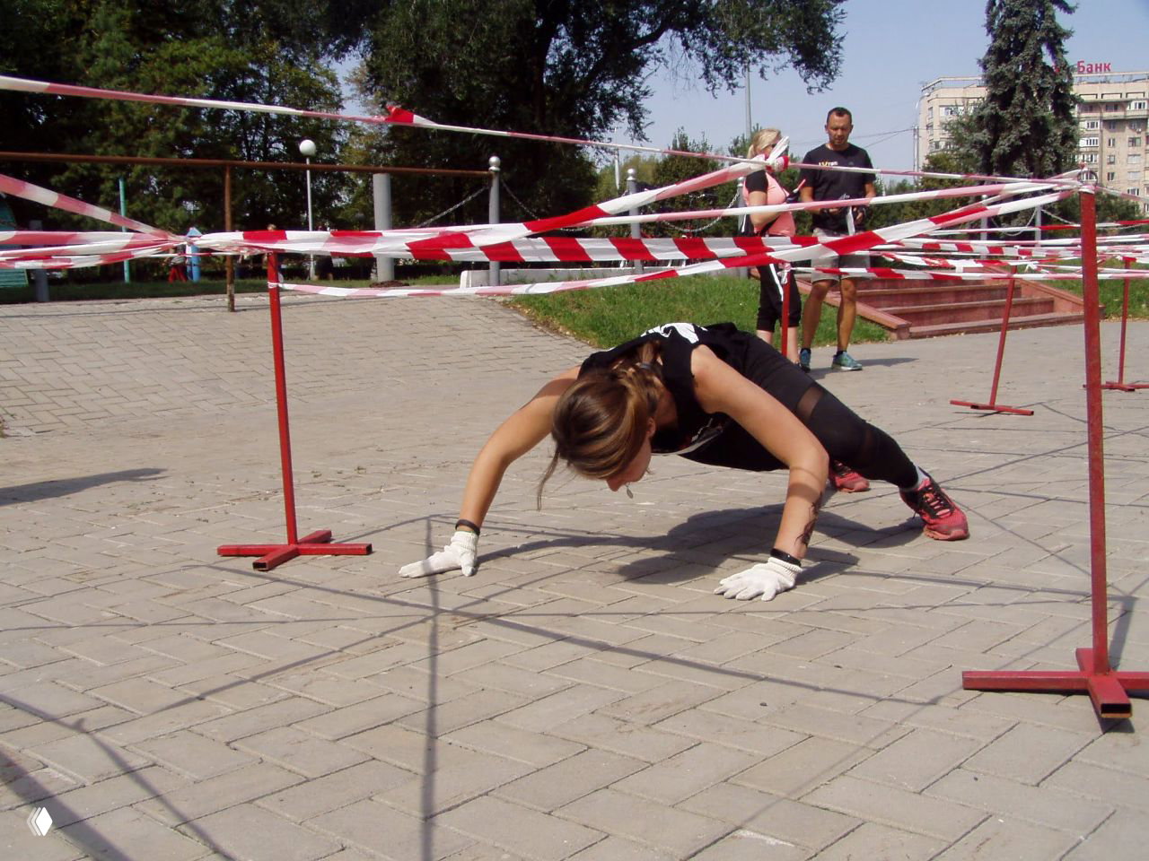 Женщина преодолевает препятствие ползком под ограждающей лентой на городской трассе Race Nation Urban, напряжённый спортивный кадр.