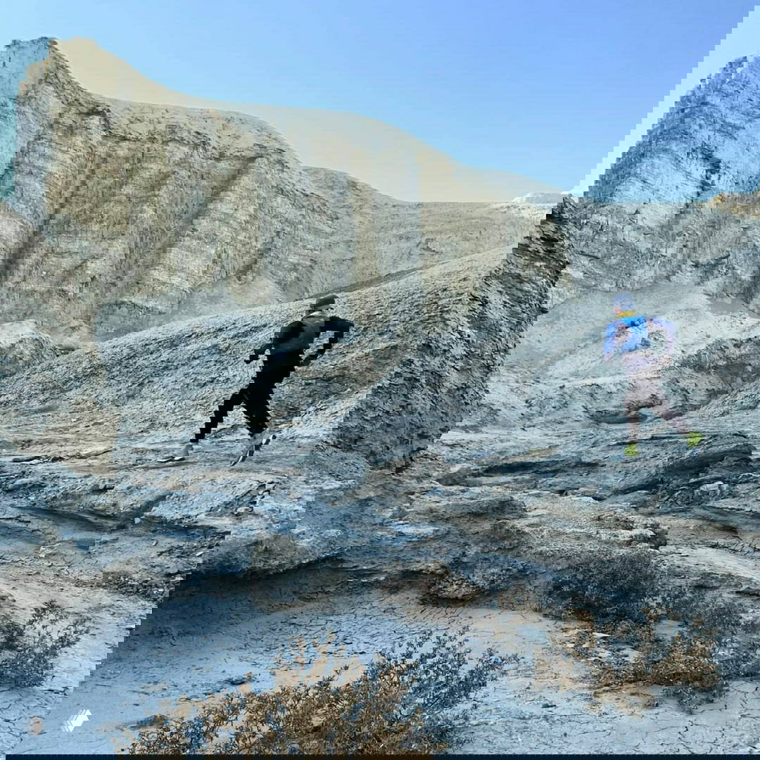 Бегун на фоне белых отвесных пород и узких ущелий — кадр показывает масштаб каньонов Алтын-Эмель и сложность маршрута для тренировки.