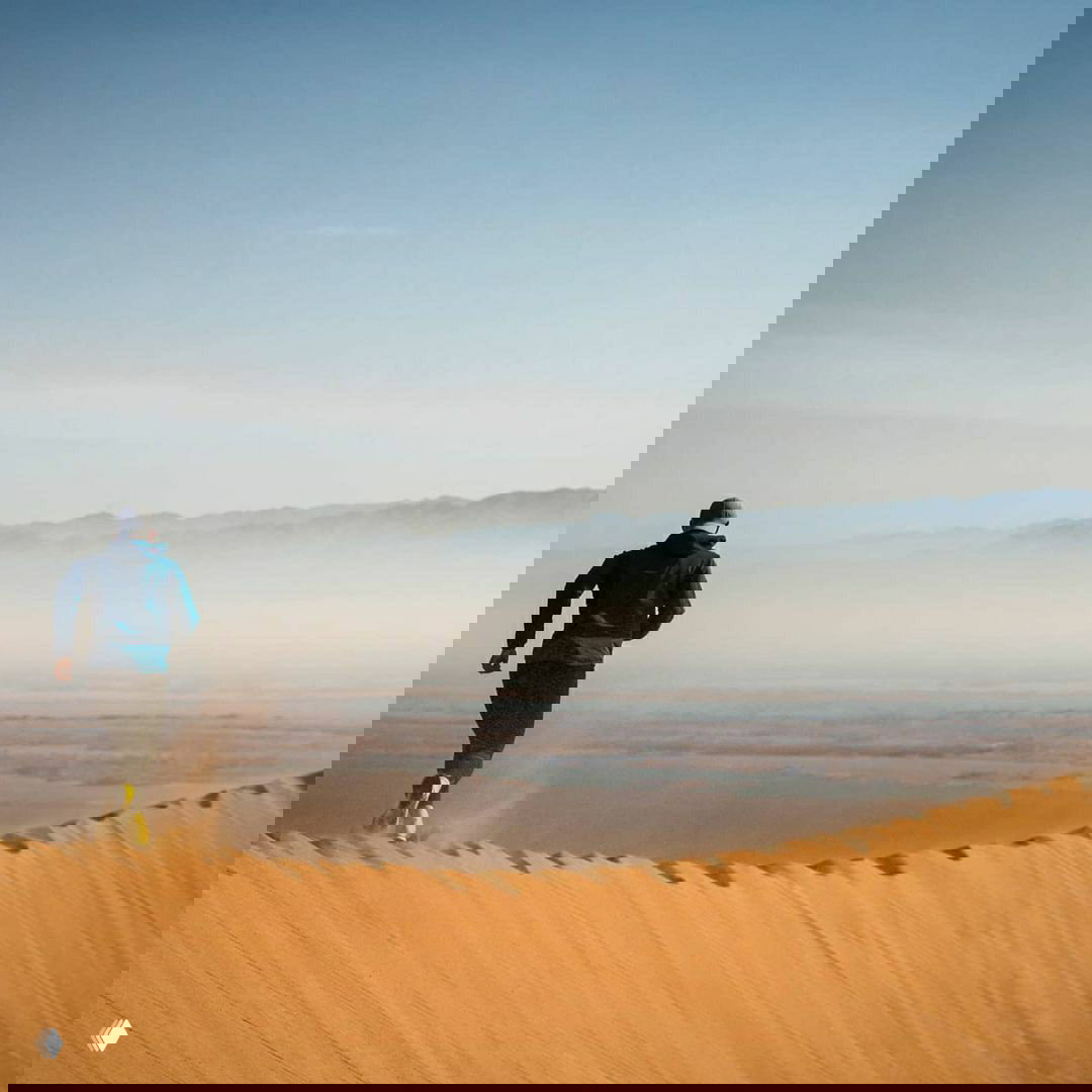 Бегун со спины на вершине бархана, видна длинная дюна и далёкий горный хребет — видовой кадр Алтын-Эмель и пустынного рельефа.