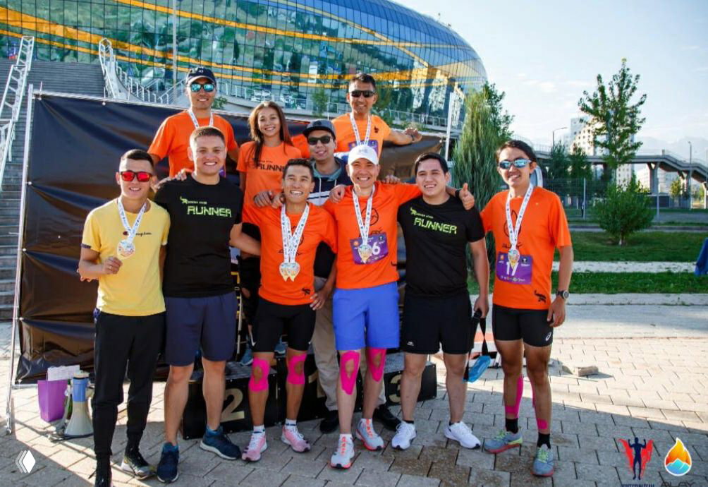 Команда бегунов в яркой форме стоит на подиуме с медалями после соревнований на открытой площадке в солнечный день.