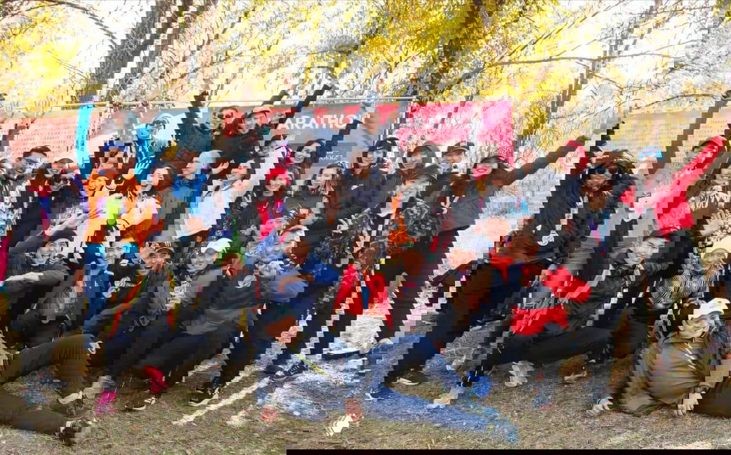 Большая группа бегунов и болельщиков позирует на осеннем финише марафона: люди с медалями и хорошим настроением.