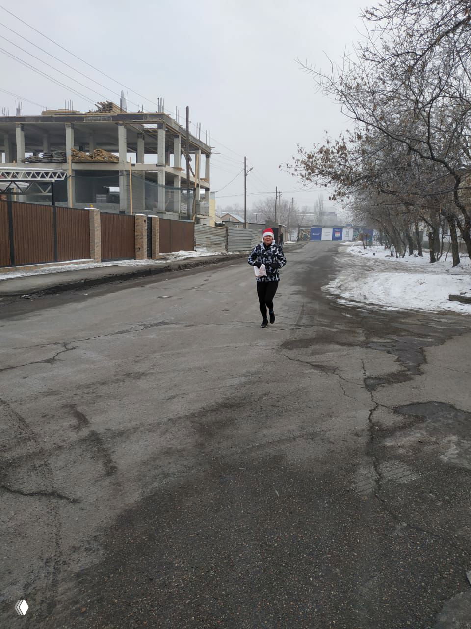 Бегун в новогодней шапке бежит по городской заснеженной улице в рамках Алматинского Новогоднего марафона, видна зимняя городская дорожная поверхность.