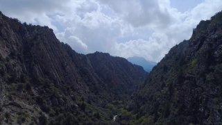 Панорамный вид горного ущелья — трасса Zaaminn Ultra на высоте около 2400 м: крутые склоны, деревья и пасмурное небо.