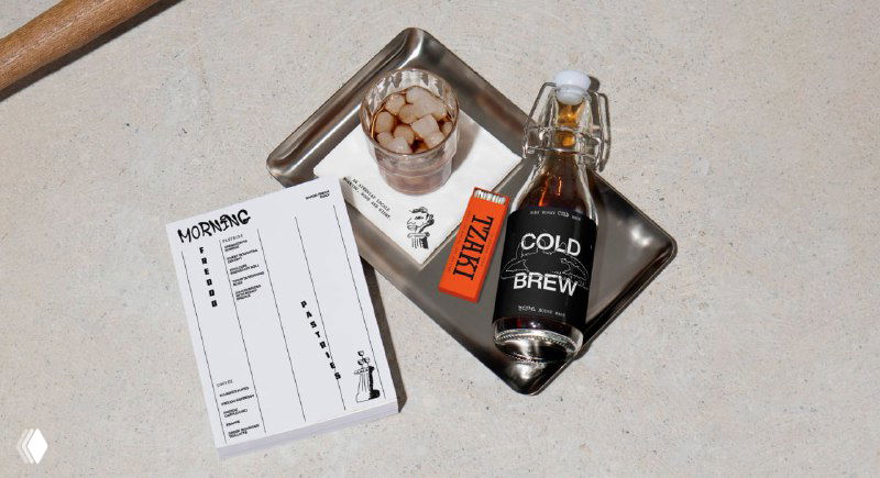 Набор брендированных предметов на столе: меню, бирки и бутылка с надписью COLD BREW, показывающий применение айдентики в интерьере и сервировке.