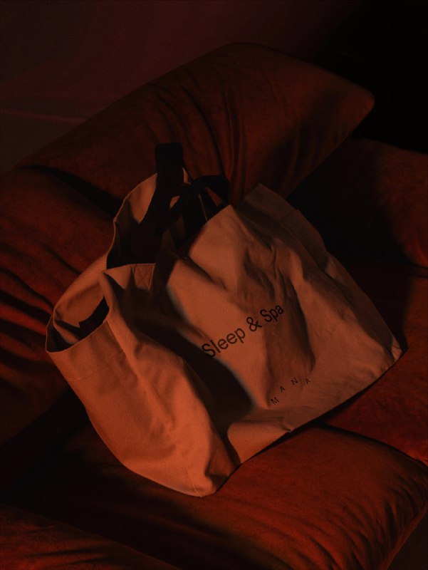 Тёплый интерьерный кадр с текстильной сумкой на кресле в красно‑оранжевой подсветке, создающий атмосферу уюта и отдыха для Mana.