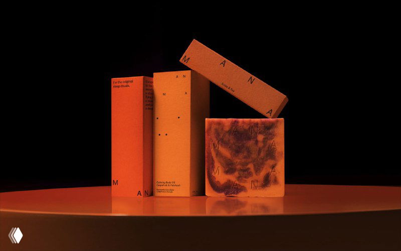 Предметная композиция на подиуме: упаковки, тубы и кусок мыла в оранжево‑красной подсветке — примеры упаковочного дизайна Mana.