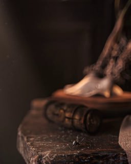 Крупный план детали анимированного натюрморта: столешница, старинная книга и маленькое насекомое на фоне тёплого рассеянного света — атмосферная студийная сцена, демонстрирующая супердетализацию и текстуры.