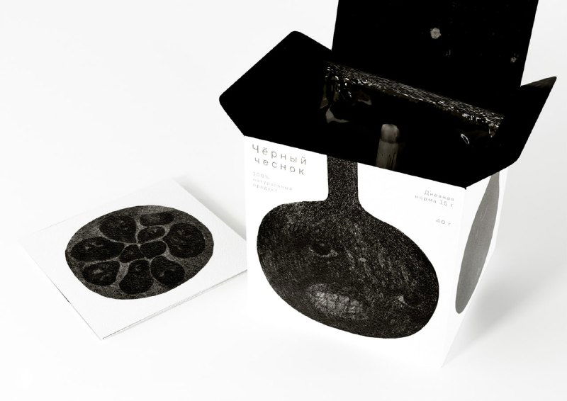 Открытая коробка и карточка с графической иллюстрацией чёрного чеснока, видна тёмная внутренняя отделка и дизайнерские вставки
