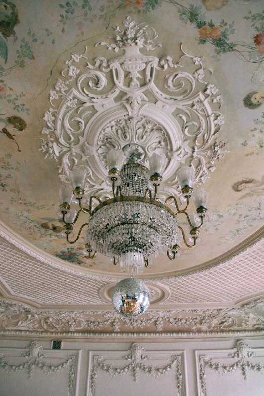 Деталь потолочной лепнины и хрустальная люстра в сочетании с зеркальным шаром — викторианская эстетика в интерьере особняка.