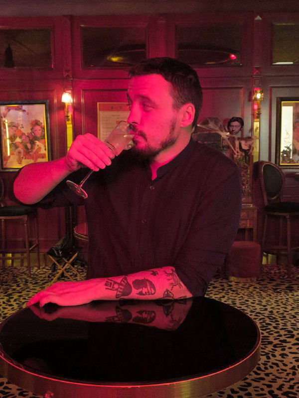 Бармен или посетитель с бокалом на фоне красной барной стены и ламп — тёплая атмосфера и винтажный стиль интерьера Chez Serge.