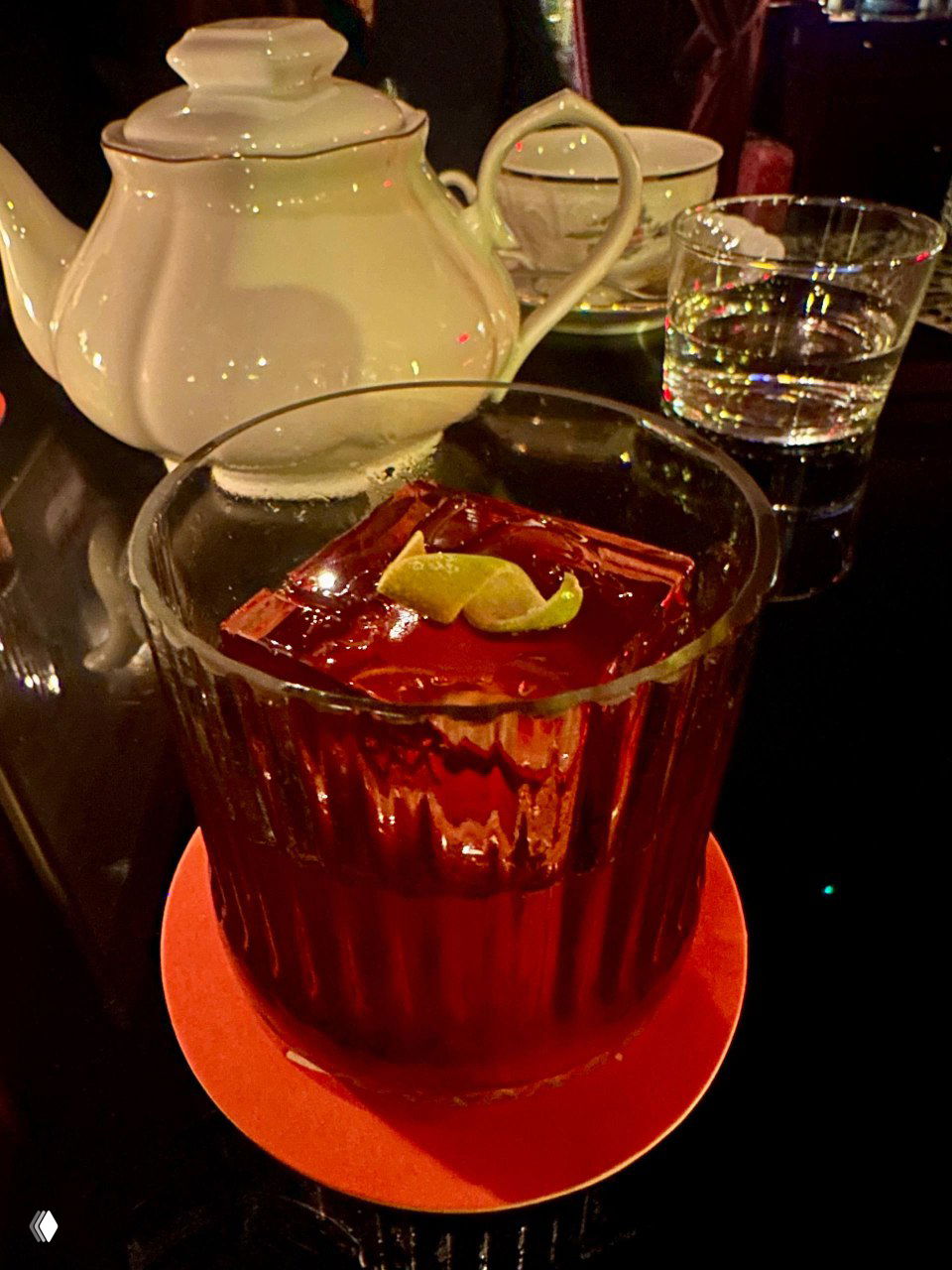 Крупный план коктейля Negroni в низком стекле с крупным кубом льда и долькой лайма на красной подставке — один из авторских напитков Chez Serge.