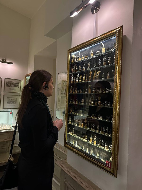 Посетительница рассматривает витрину с маленькими стеклянными флаконами и экспонатами, связанные с историей алкоголя и напитков.