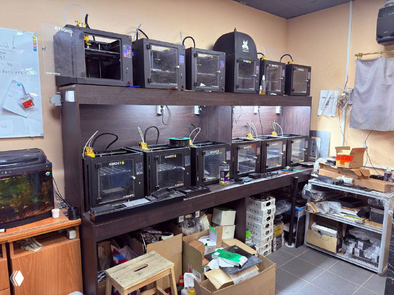 Стеллаж с тремя десятками настольных и закрытых 3D‑принтеров в лабораторной зоне для прототипирования и мелкосерийного производства.