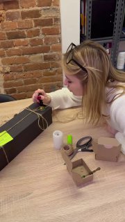 Крупный план: женщина накручивает украшение на коробку, рабочий стол с инструментами и материалами для упаковки подарков.