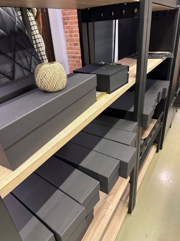 Ряд сложенных черных подарочных коробок на металлической полке, видна готовая складская зона с корпоративными наборами.