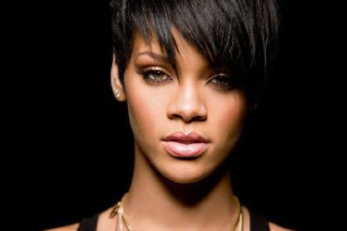 Крупный план Рианны с короткой стрижкой и выразительным макияжем; студийный тёмный фон подчёркивает черты лица и укладку.