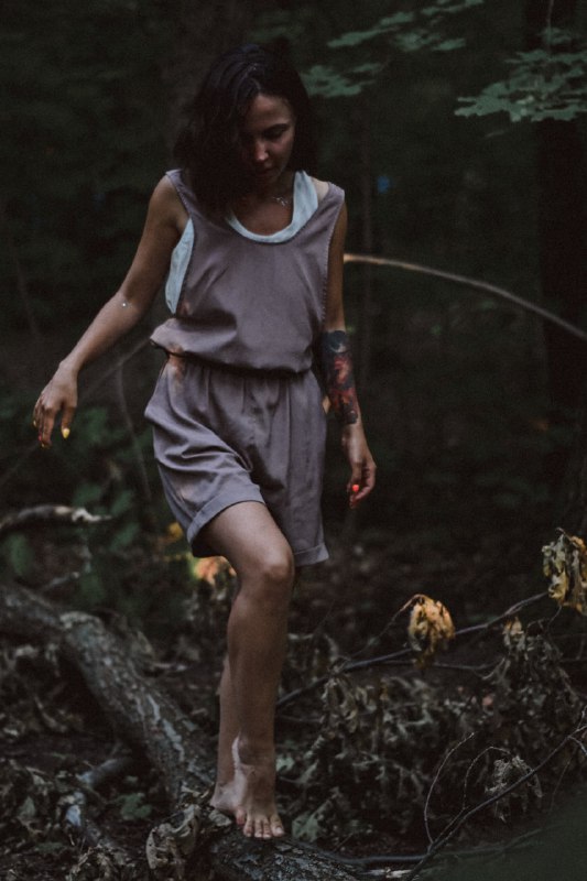 Девушка в лёгком платье идёт босиком по лесной подстилке, естественная поза и тёплая зелёная гамма подчёркивают атмосферу уединения и искренности.