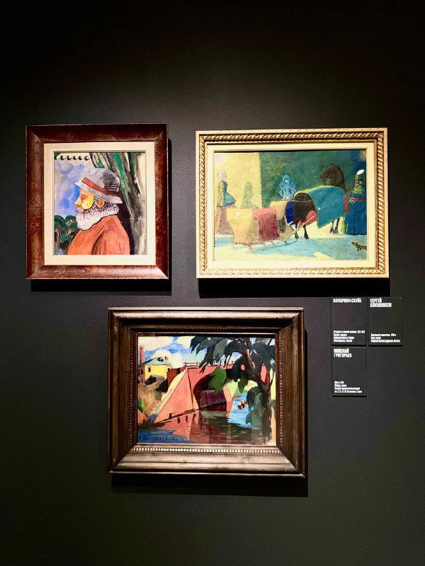 Три небольшие картины в рамках на темной стене: портреты и пейзаж в рамах, рядом видны музейные таблички и подписи.