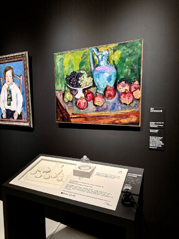 Натюрморт с гранатами и портрет рядом; внизу — тактильный стенд с рельефом картины и пояснительной табличкой для слабовидящих.