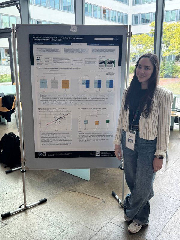 Автор стоит рядом с постером конференции, на котором графики и блоки текста; холл с панорамными окнами и дневным светом.