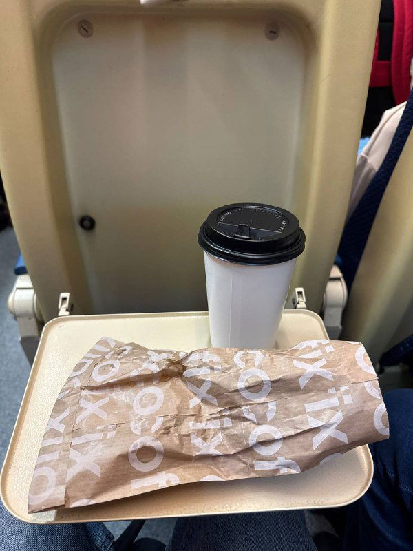 Откидной столик в поезде с одноразовым стаканом кофе и упакованной булочкой на столике — момент поездки и перекуса в пути