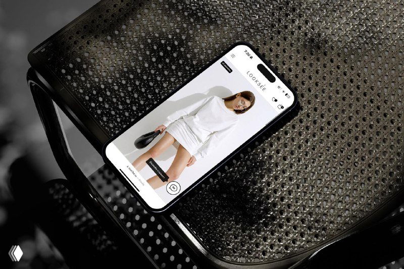 Фотография мобильного телефона на стуле с открыткой сайта магазина одежды — пример e‑commerce макета в подборке стильных сайтов.