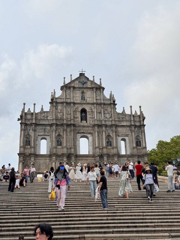 Фотография руин храма Святого Павла при дневном свете: широкая лестница, множество туристов и фронтон старой фасады-стены — визитная карточка Макао.