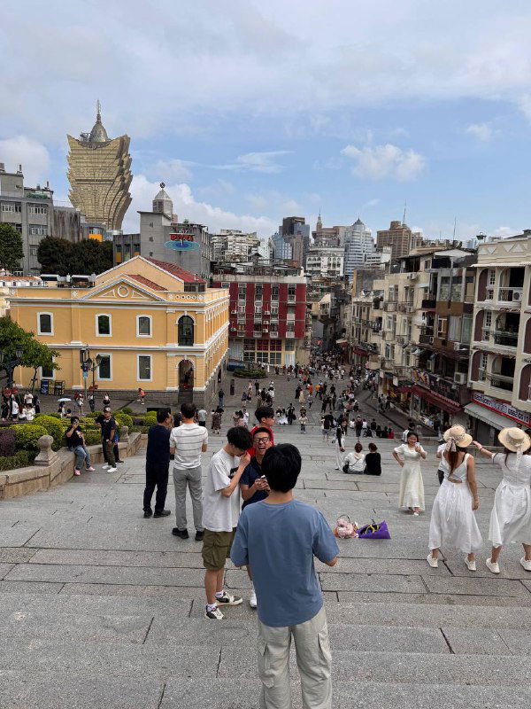 Вид сверху на широкую лестницу и разноцветные колональные дома внизу: живые уличные сцены и туристы на прогулке по старому району Макао.