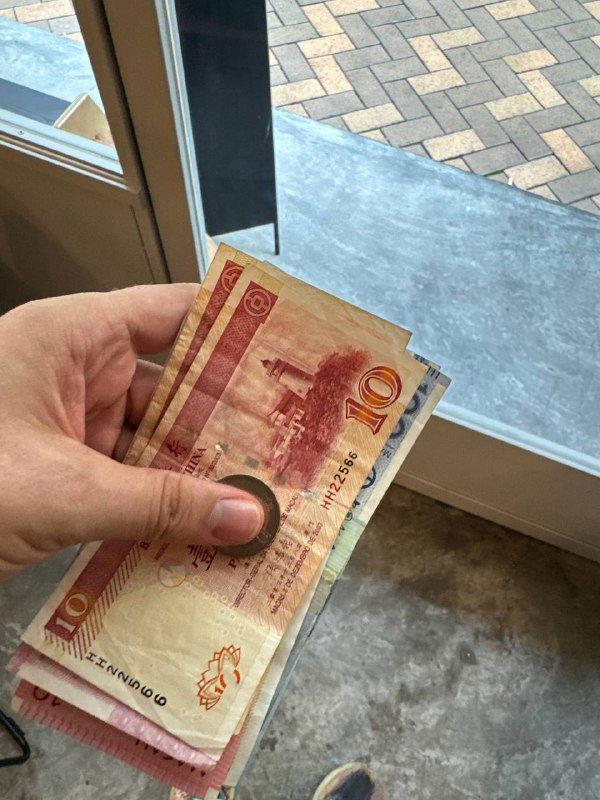 Рука держит пачку банкнот у окна — снимок с крупным планом денег, вероятно, купюр местной валюты после выигрыша или в быту путешественника.