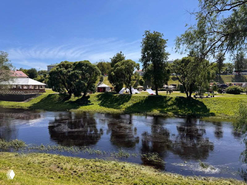 Речная заводь с зелёными деревьями и ясным отражением в воде, спокойный летний пейзаж на окраине исторического центра.