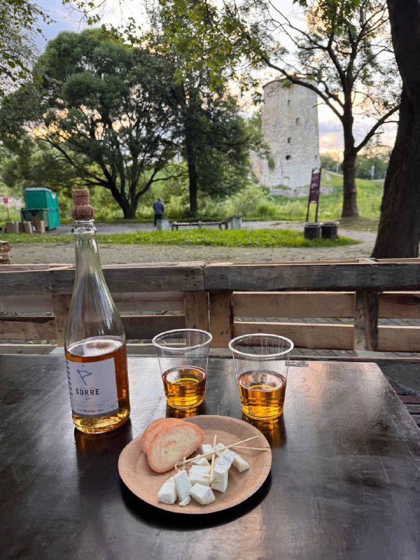 Столик в уличном кафе с бутылкой, двумя стаканами и закуской на деревянной поверхности; атмосфера локального общепита.