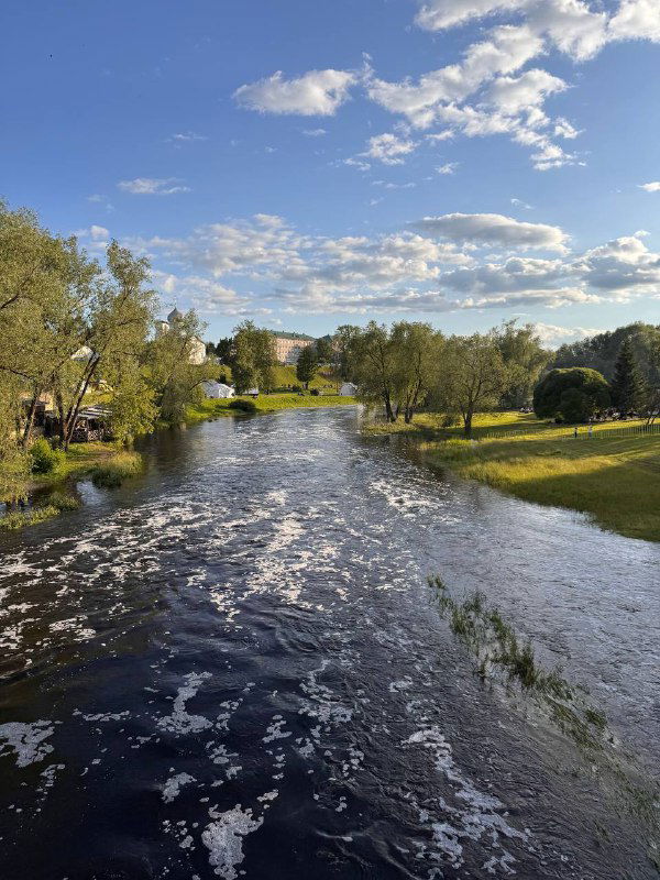 Река с плавным изгибом, деревья по берегам и лёгкие облака в небе; панорамный вид на водную часть Пскова вечером.