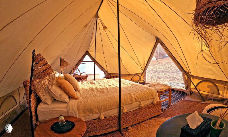 Интерьер палатки с уютной кроватью, декоративными подушками и мягким освещением; стильный глэмпинг для комфортной ночёвки.