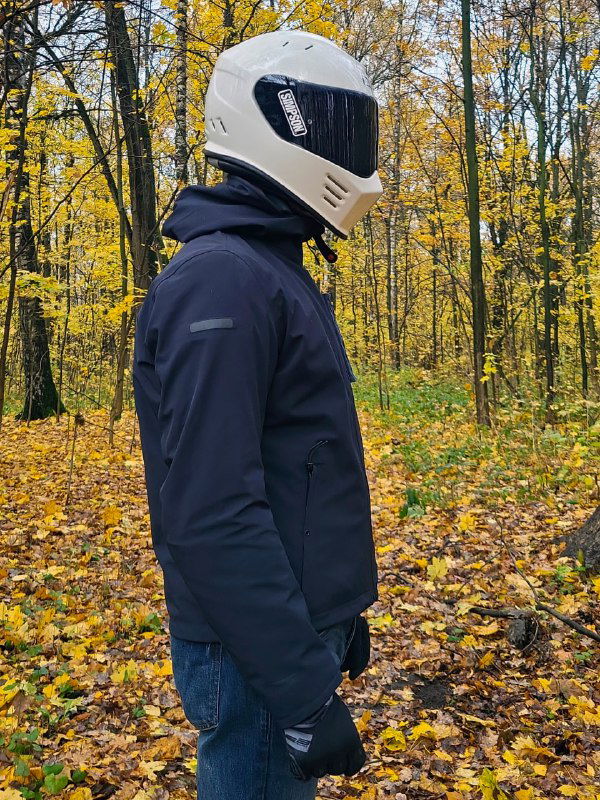 Боковой профиль куртки Dainese Corso AbsØluteshell Pro: капюшон, рукав и посадка на мотоциклисте на фоне жёлтой осенней листвы.